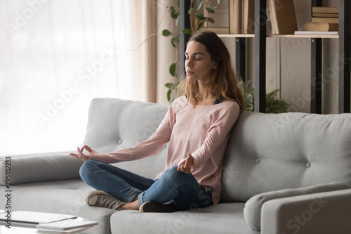 Healthy calm girl sit on sofa meditating doing yoga exercise