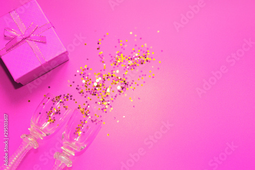 Pink background with decorative metallic stars, two vintage glasses and a gift box. Holiday theme backdrop. Festive and party concept