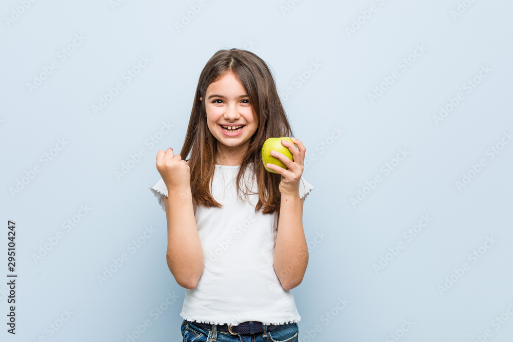 Little caucasian girl holding a green apple cheering carefree and excited. Victory concept. Little caucasian girl holding a green apple cheering carefree and excited. Victory concept.