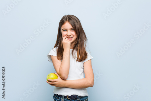 Little caucasian girl holding a green apple relaxed thinking about something looking at a copy space.
