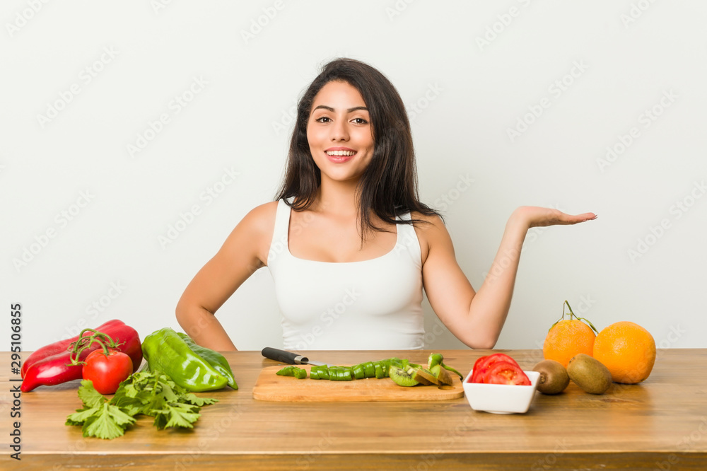 Young curvy woman preparing a healthy meal showing a copy space on a palm and holding another hand on waist. Young curvy woman preparing a healthy meal showing a copy space on a palm and holding another hand on waist.