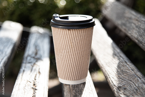 A paper coffee cup with cap on a bench