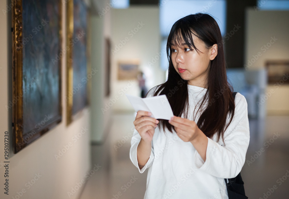 Chinese woman standing with guide-book near painting in baguette