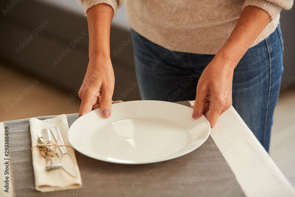 Close-up of woman putting the white plate on the table and serving the table before dinner Close-up of woman putting the white plate on the table and serving the table before dinner