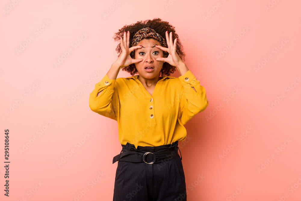 Young african american woman against a pink background keeping eyes opened to find a success opportunity. Young african american woman against a pink background keeping eyes opened to find a success opportunity.