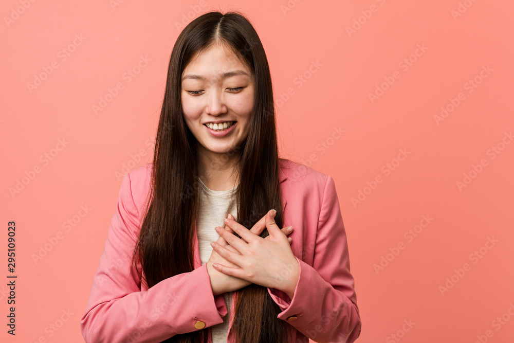 Young business chinese woman wearing pink suit laughing keeping hands on heart, concept of happiness. Young business chinese woman wearing pink suit laughing keeping hands on heart, concept of happiness.