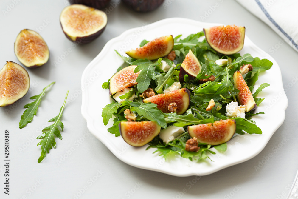 Salad with arugula, figs, cheese, walnut and honey. Autumn salad with figs and cheese on a white plate. Salad with arugula, figs, cheese, walnut and honey. Autumn salad with figs and cheese on a white plate.