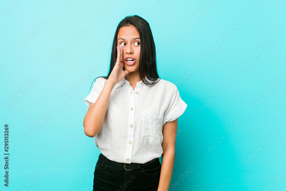 Young hispanic cool woman against a blue wall is saying a secret hot braking news and looking aside Young hispanic cool woman against a blue wall is saying a secret hot braking news and looking aside