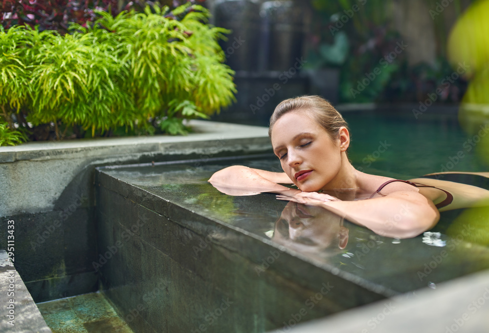 Fototapeta Zdrowa kobieta relaksuje outdoors w słonecznym i roślinnym otaczającym pływackim basenie luksusowy kurort podczas tropikalnego wakacje na Bali