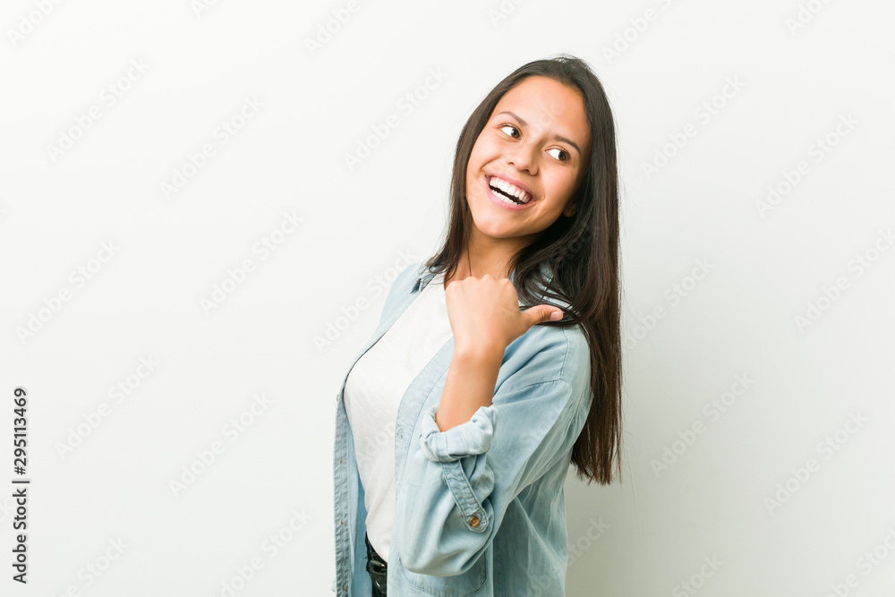 Young hispanic woman points with thumb finger away, laughing and carefree. Young hispanic woman points with thumb finger away, laughing and carefree.