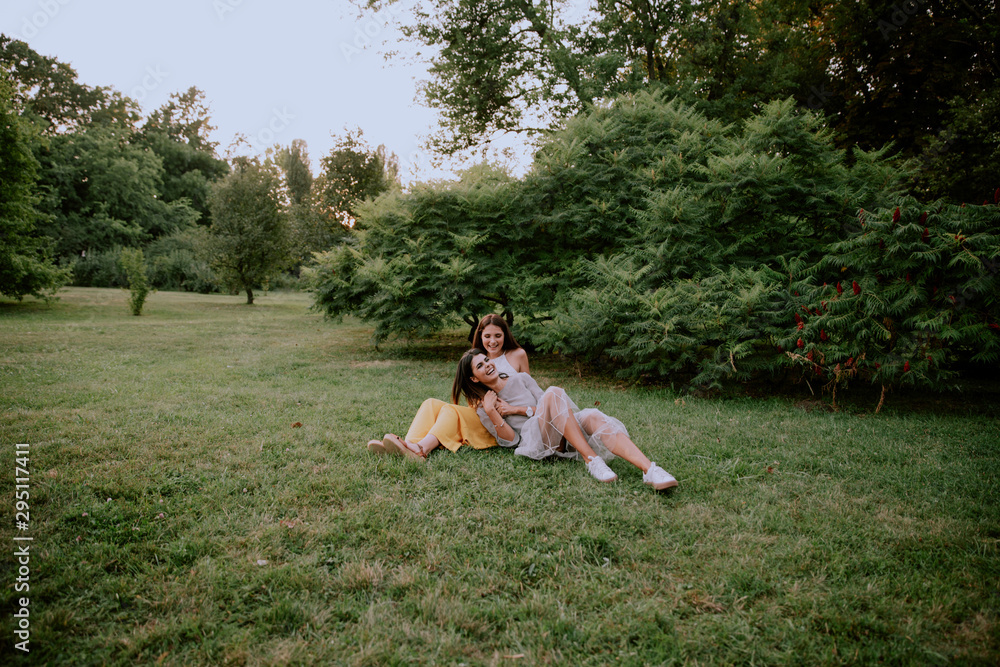 Attractive two ladies in the park enjoying the time together sitting down on the grass and chatting smiling large beside Attractive two ladies in the park enjoying the time together sitting down on the grass and chatting smiling large beside