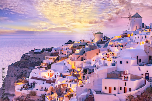 Beautiful view of picturesque Oia village with traditional white architecture and windmills in Santorini island in Aegean sea at sunset, Greece. Scenic travel background.