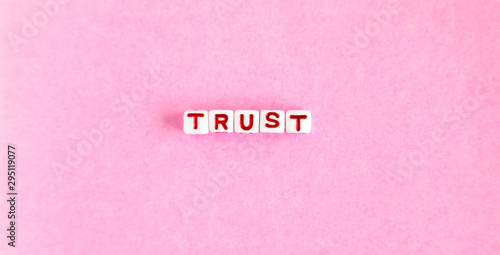 Word "Trust" made out of colorful beads on pink background. Overhead view.