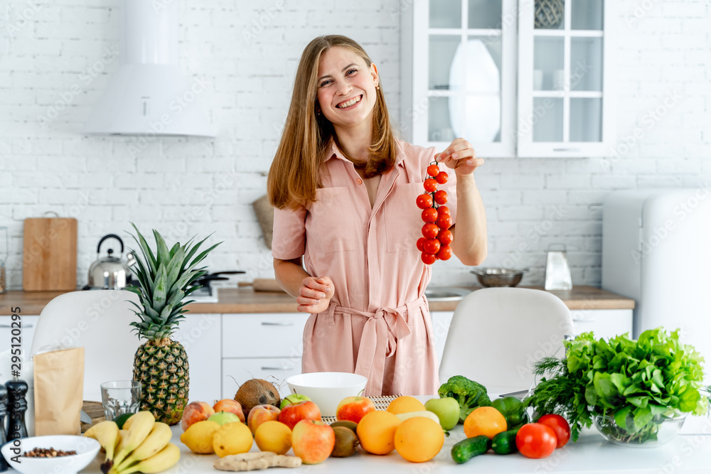 Woman in kitchen ready to prepare meal with vegetables and fruits. Woman is holding tomatoes. Kitchen background. Healthy food. Vegans. Vegeterian. Banch of tomatoes.