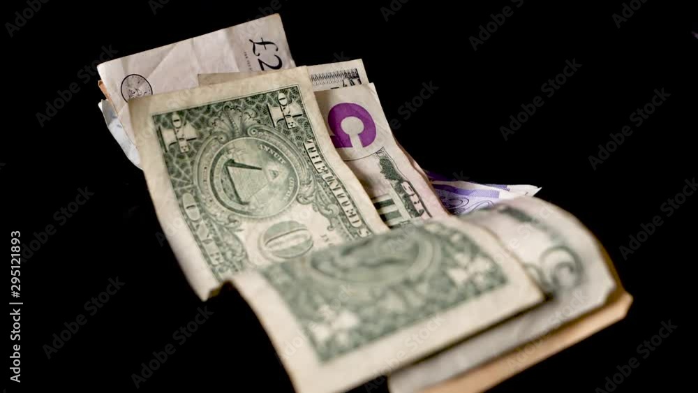 Pile of dollars and pounds of bills falling on table in front of black background Pile of dollars and pounds of bills falling on table in front of black background