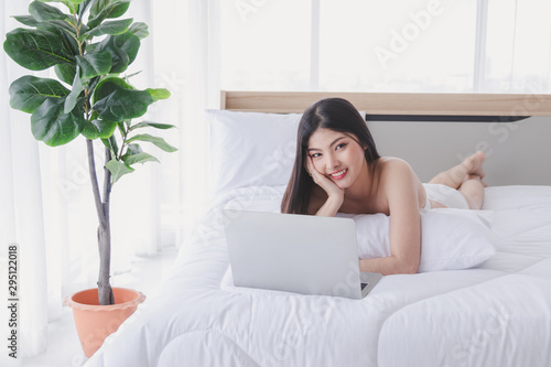 Charming woman smiles and lies on the bed with labtop in bedroom