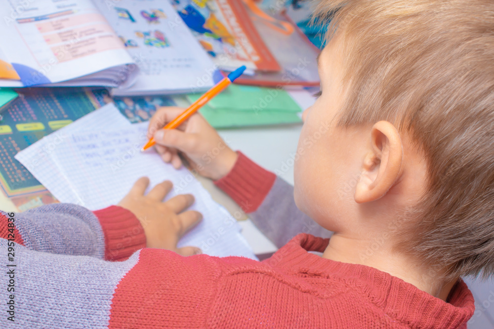 A boy writes English words by hand on traditional white paper in a notebook. The boy writes his first test on English. Child writing, spelling and education. Boy learns english. English writing skills A boy writes English words by hand on traditional white paper in a notebook. The boy writes his first test on English. Child writing, spelling and education. Boy learns english. English writing skills