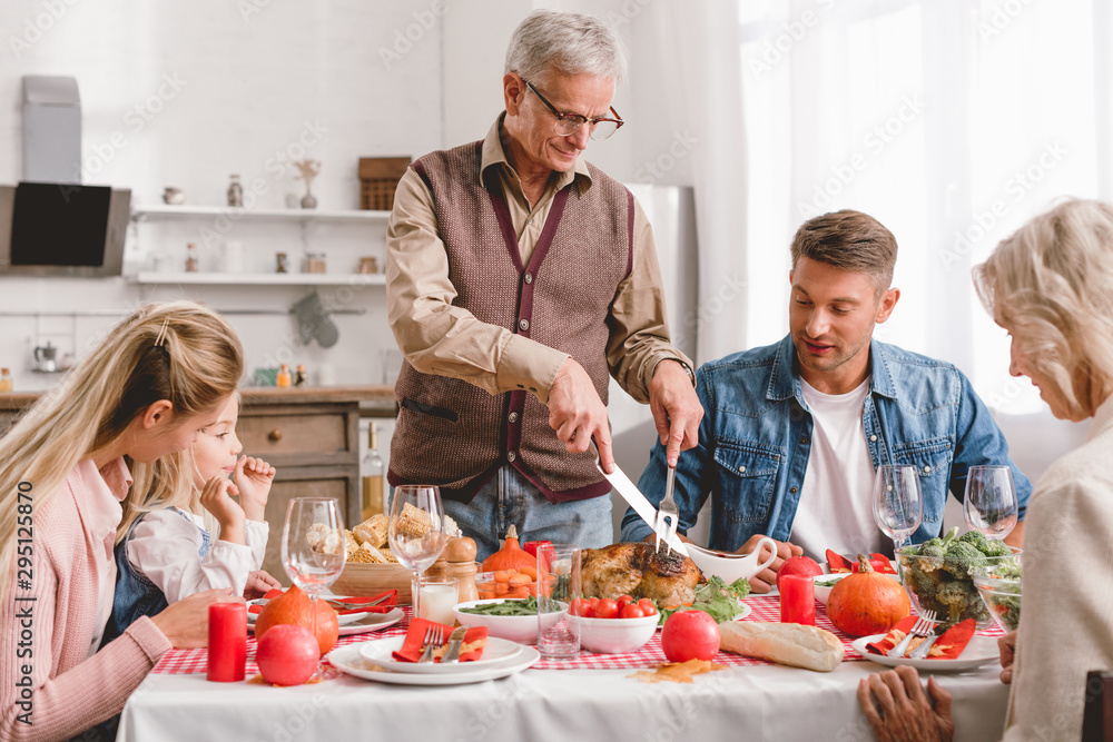 family members sitting at table and grandfather cutting tasty turkey in Thanksgiving day family members sitting at table and grandfather cutting tasty turkey in Thanksgiving day