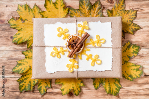 Gift box in kraft packaging. Mockup torn paper for your notes. Autumn bright dry leaves.Yellow knitted sweater on a wooden background. cozy autumn concept. flat lay.