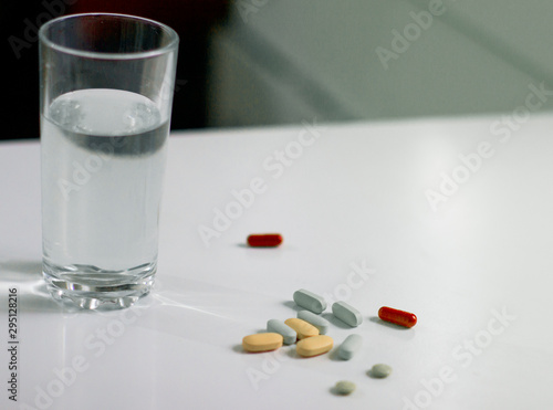 Multi-colored pills and a glass of water on a white table. Many pill of vitamin and medicine.
