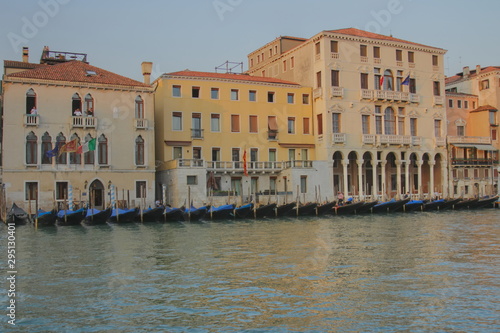 Gondolas stand in a row near an old building in Venice, view through the canal, evening light