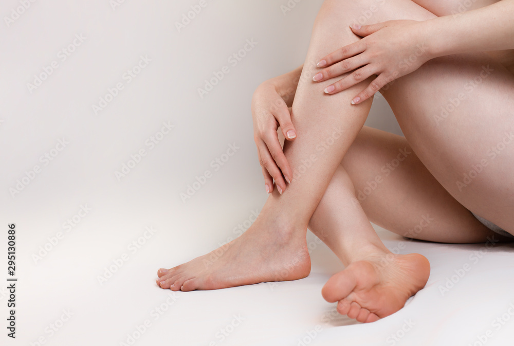 The concept of varicose disease and medicine. The woman sits with her slender legs crossed and her arms around them. White background. Copy space The concept of varicose disease and medicine. The woman sits with her slender legs crossed and her arms around them. White background. Copy space