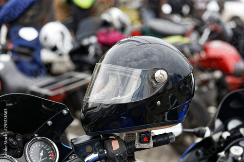 Closeup bkack moto helmet on motorcycle handlebars and motorbikes on blurred background