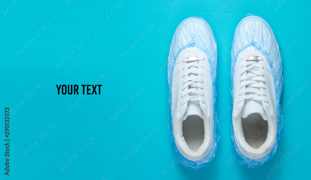 White sneakers in boot covers on blue background. Top view. Minimalism. Copy space - obrazy, fototapety, plakaty 
