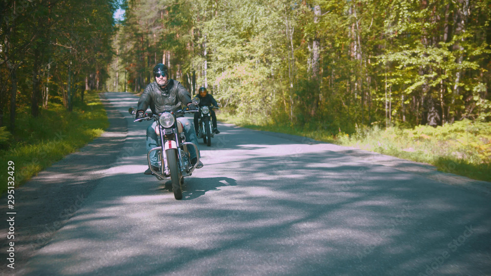 Obraz premium Dwóch motocyklistów jedzie zakurzoną drogą w lesie
