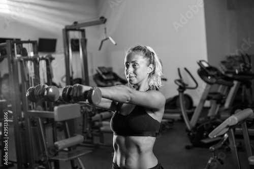 Young fit woman in sportswear is training with dumbbells in the gym. Healthy lifestyle concept. Body training with free weights