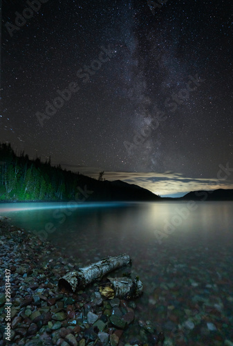 The milky way and stars lighting up on top of the Lake Macdonald  and two pieces of wood washed up on the beach  Montana.