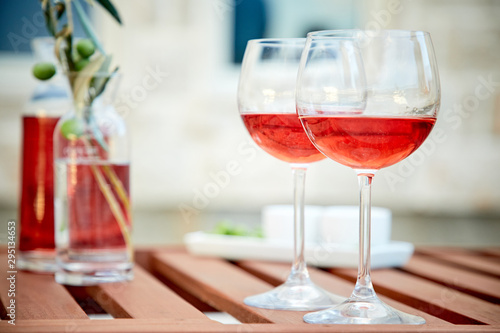 two glasses of rose wine with olives against blue water on a pier..