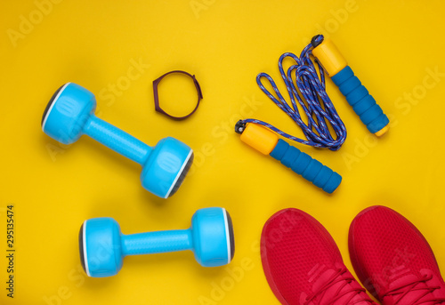 Minimalistic sport still life. Sports outfit. Red sports shoes for training and blue plastic dumbbells, jump rope, smart bracelet on a yellow background. Top view © splitov27
