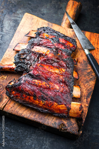 Barbecue burnt chuck beef ribs marinated with hot chili sauce as closeup on an old rustic wooden cutting board