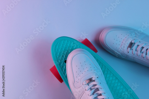 White sneakers on plastic mini cruiser board with blue pink neon gradient ligh. Top view