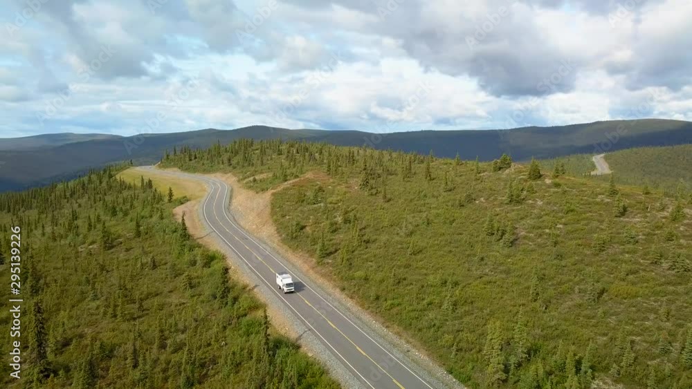 Aerial, reverse, drone shot, panning towards a camper van, driving on the top of the world highway, tarmac road, on high hills, in Alaskan wild and arctic tundra, on a partly sunny day, in Alaska, USA Aerial, reverse, drone shot, panning towards a camper van, driving on the top of the world highway, tarmac road, on high hills, in Alaskan wild and arctic tundra, on a partly sunny day, in Alaska, USA