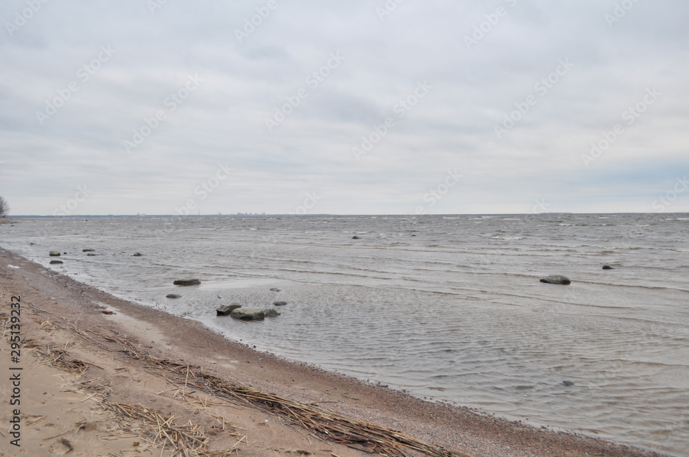 gray sky, gray water, brown sand, stones in the water