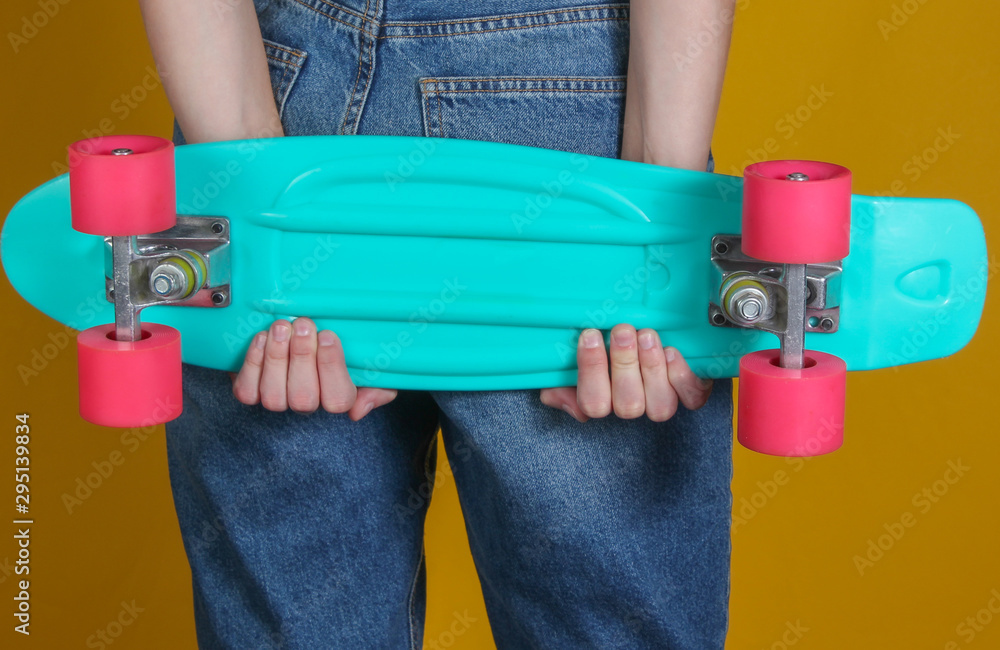 Young slim woman in jeans holds plastic cruiser board in her hands on yellow background. Youth hipster fashion. Summer fun. Studio shot. Crop photo