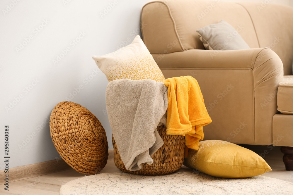 Wicker basket with color blankets and pillows near beige sofa
