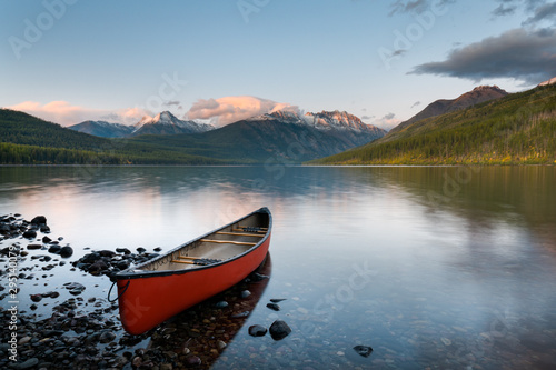 A canoe sitting still at the beach of the Kinktla Lake, with the sunset hitting the snow covered mountains at Kinktla Lake, Montana.