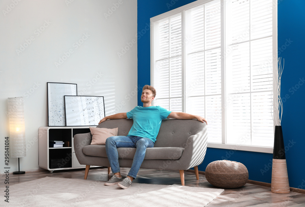 Happy young man resting on sofa under air conditioner at home Happy young man resting on sofa under air conditioner at home