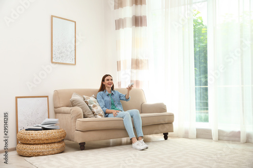 Happy young woman switching on air conditioner with remote control at home