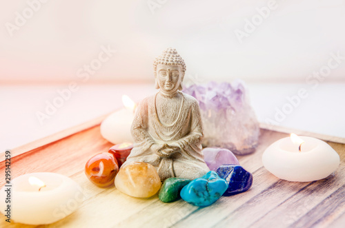 Fotografija All seven chakra colors crystals stones around sitting Buddha figurine on natural wooden tray