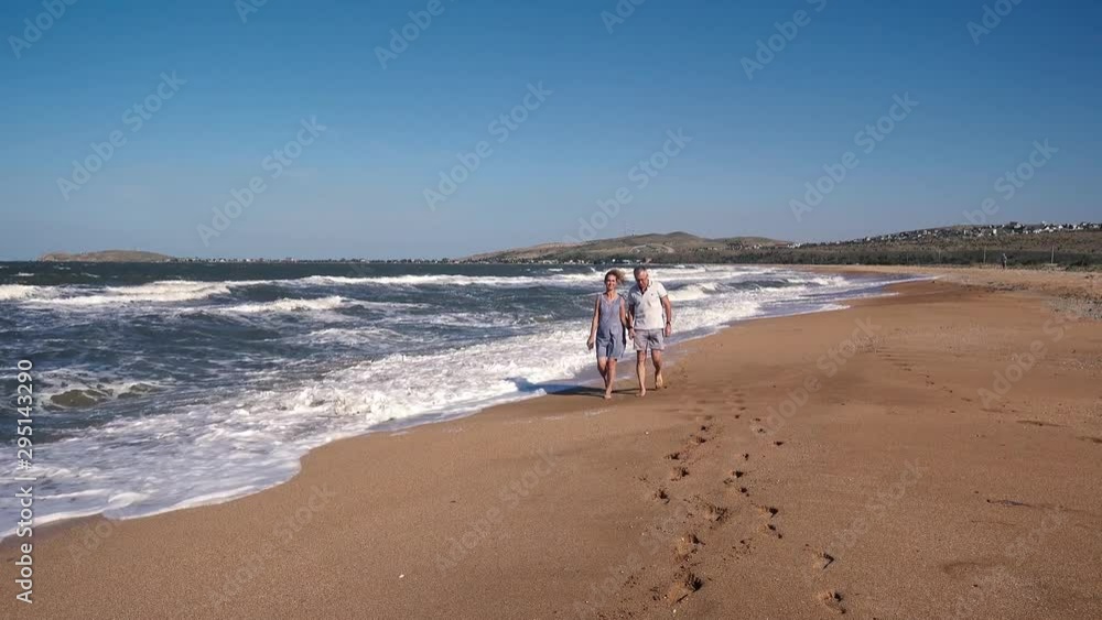 People, a man and a woman walk along the sandy beach and admire the sea waves on a Sunny summer day. People, a man and a woman walk along the sandy beach and admire the sea waves on a Sunny summer day.