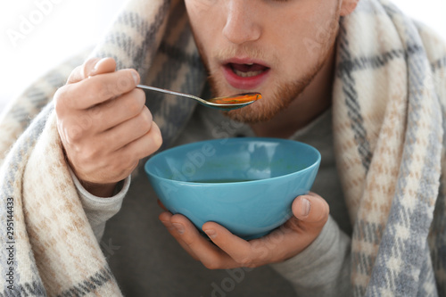 Sick young man eating soup to cure flu, closeup