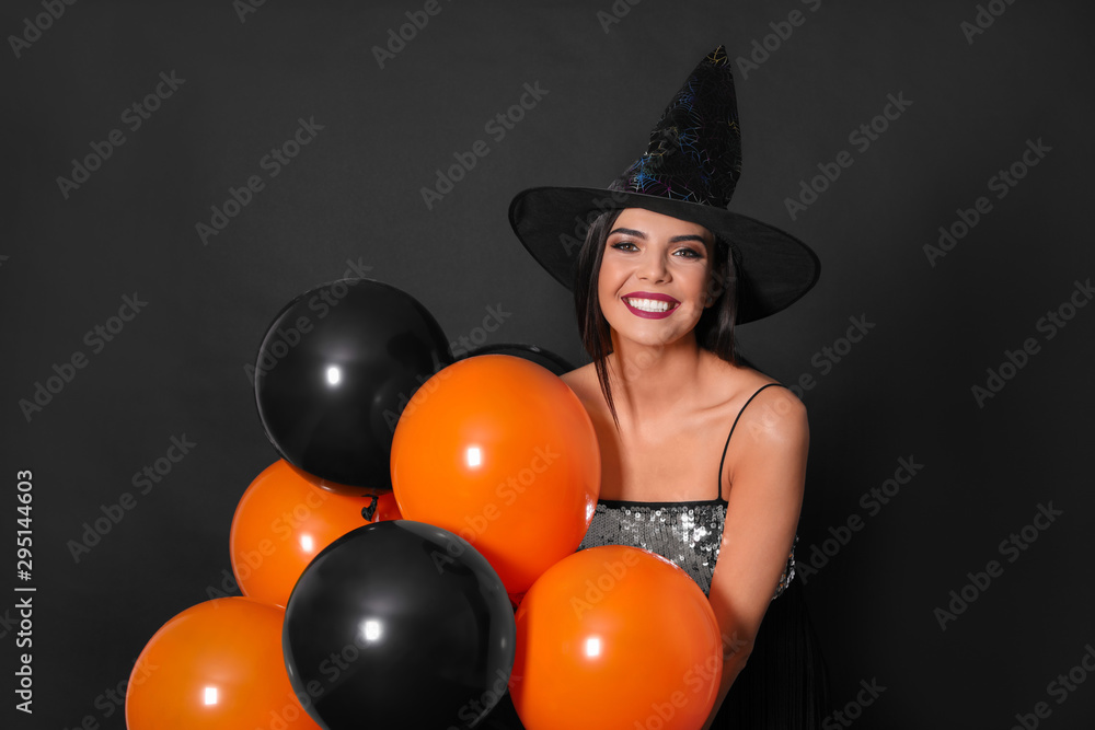 Beautiful woman wearing witch costume with balloons for Halloween party on black background Beautiful woman wearing witch costume with balloons for Halloween party on black background