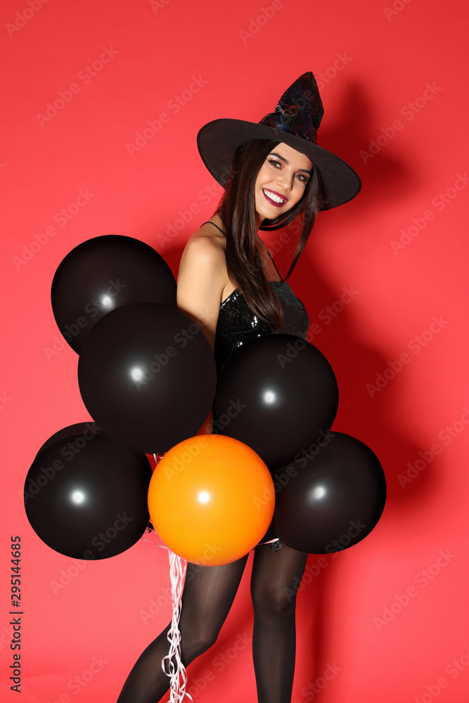 Beautiful young woman wearing witch costume with balloons for Halloween party on red background