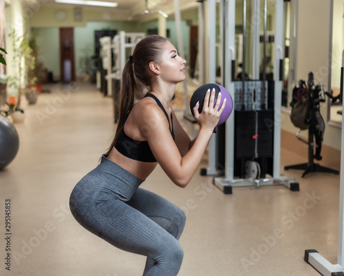 Functional Training Concept. Young fit woman in sportswear crouches with medicine ball in her hands at gym