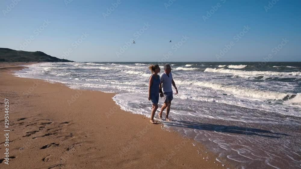 People, a man and a woman walk along the sandy beach and admire the sea waves on a Sunny summer day. People, a man and a woman walk along the sandy beach and admire the sea waves on a Sunny summer day.