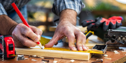 Adult carpenter craftsman with a pencil and the carpenter's square trace the cutting line on a wooden table. Construction industry, housework do it yourself. Stock photography.